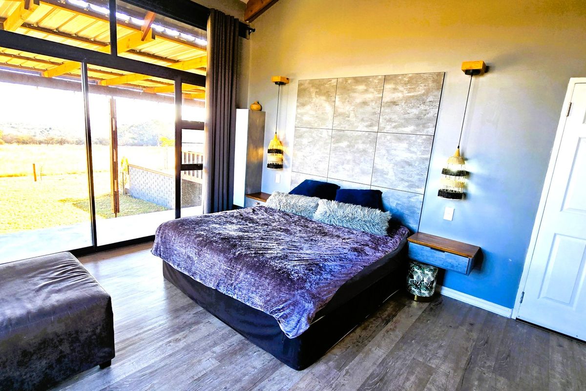 Spacious bedroom featuring exposed timber ceiling beams, modern feature wall paneling, and large sliding glass doors providing direct access to the outdoor area.