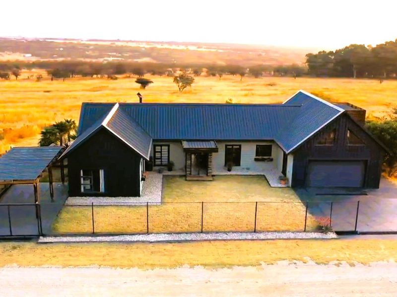 Aerial view of a modern farmhouse-style residence featuring a dark metal roof, attached garage, and covered patio set within a rural landscape.