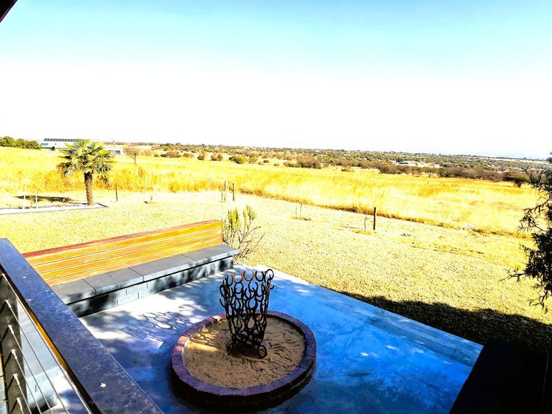 An elevated outdoor patio featuring a concrete floor, built-in timber seating, and a central fire pit, overlooking a vast open landscape.