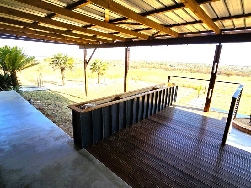 Spacious covered patio featuring timber decking, a corrugated metal roof, and a built-in planter box, offering expansive views of the surrounding landscape.