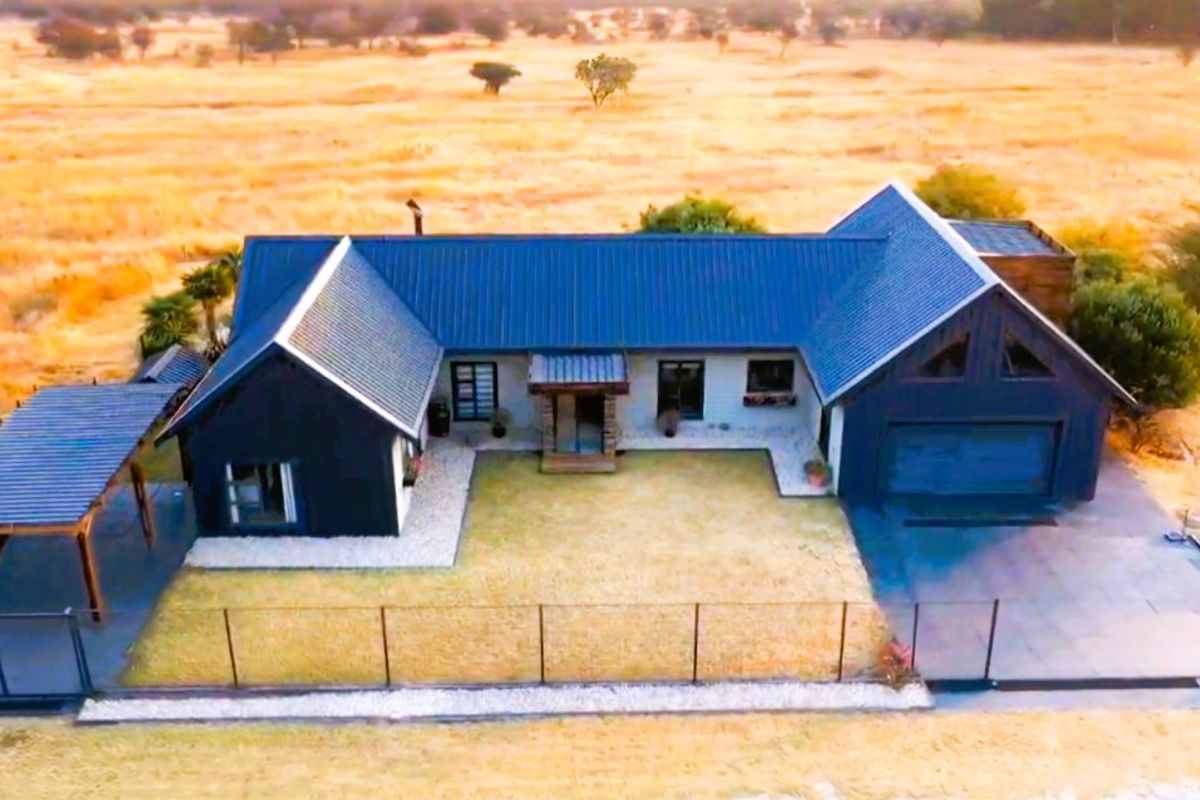 Aerial view of a modern house featuring a dark metal roof, attached garage, and a carport, set within a rural landscape.