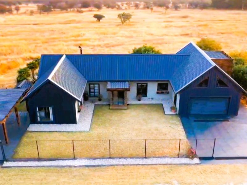 Aerial view of a modern house featuring a dark metal roof, attached garage, and a carport, set within a rural landscape.