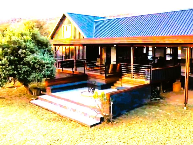 Rear exterior view of the house featuring a spacious timber deck, steel balustrades, and a sunken fire pit area set within a natural landscape.