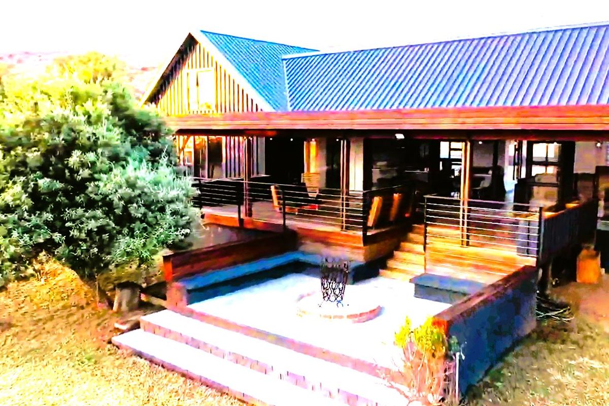 Rear exterior view featuring a spacious timber deck, metal roof, and a sunken fire pit area with stone paving.