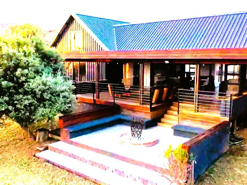 Rear exterior view featuring a spacious timber deck, metal roof, and a sunken fire pit area with stone paving.