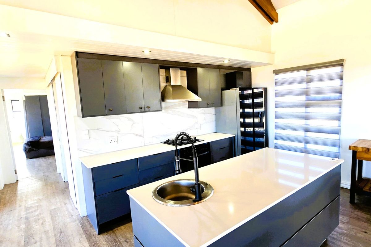 Modern kitchen featuring dark cabinetry, stone countertops, a central island with a prep sink, and high-quality built-in appliances under a vaulted ceiling.
