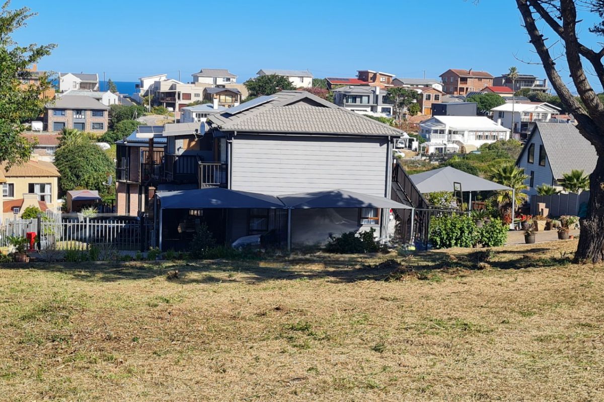 A view of the rear elevation of a residential property featuring a tiled roof, timber cladding, and an attached carport, set within a coastal neighborhood.