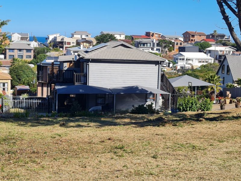 A view of the rear elevation of a residential property featuring a tiled roof, timber cladding, and an attached carport, set within a coastal neighborhood.