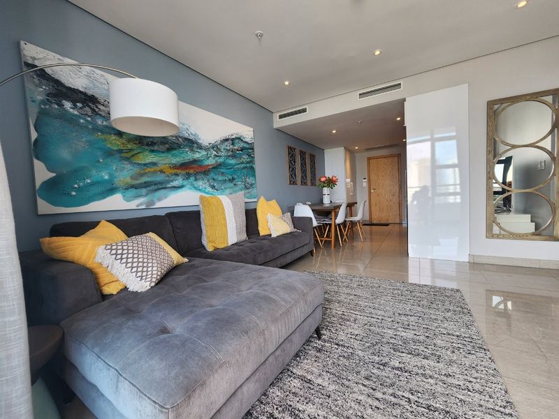 A modern open-plan living and dining area featuring sleek tiled flooring, recessed lighting, and integrated ducted air conditioning.