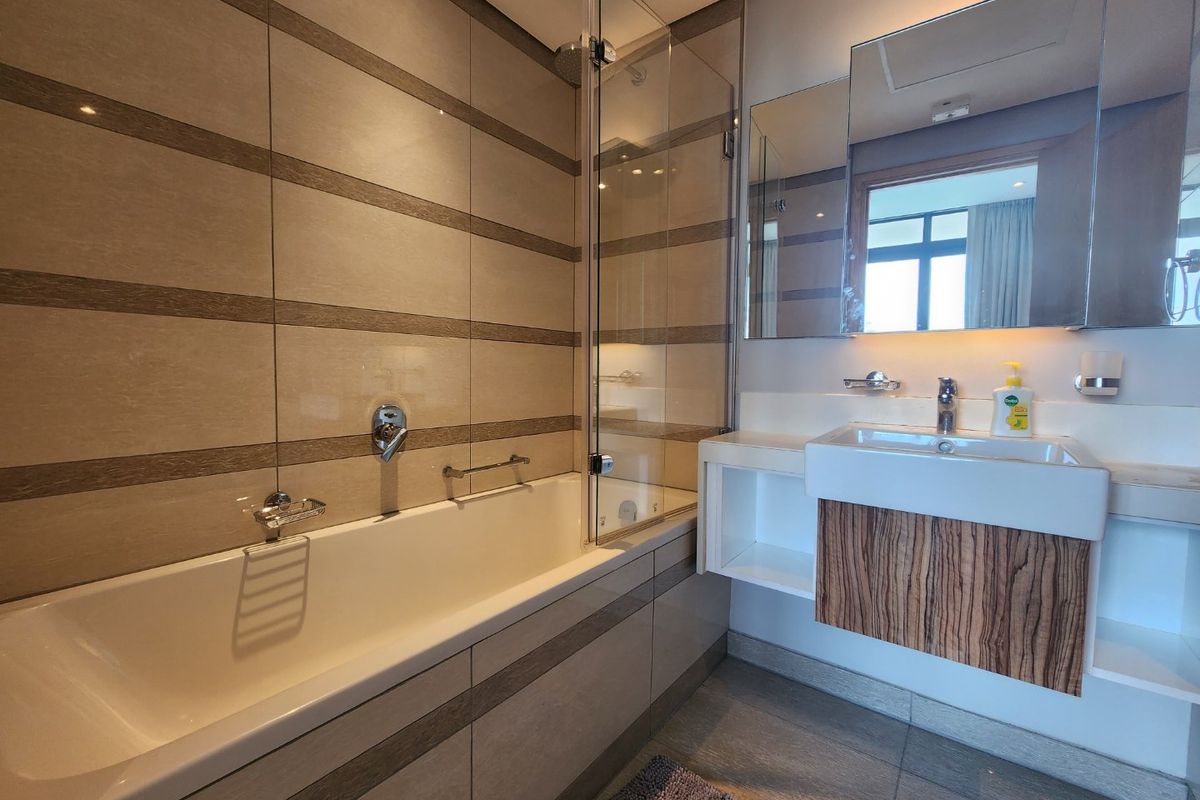 Modern bathroom featuring a built-in bathtub with glass screen, wall-mounted vanity with integrated basin, and contemporary tiled finishes.
