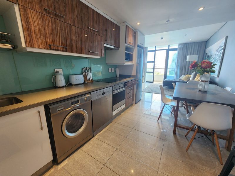 Modern open-plan kitchen and living area featuring sleek cabinetry, integrated appliances, tiled flooring, and direct access to a balcony with city views.