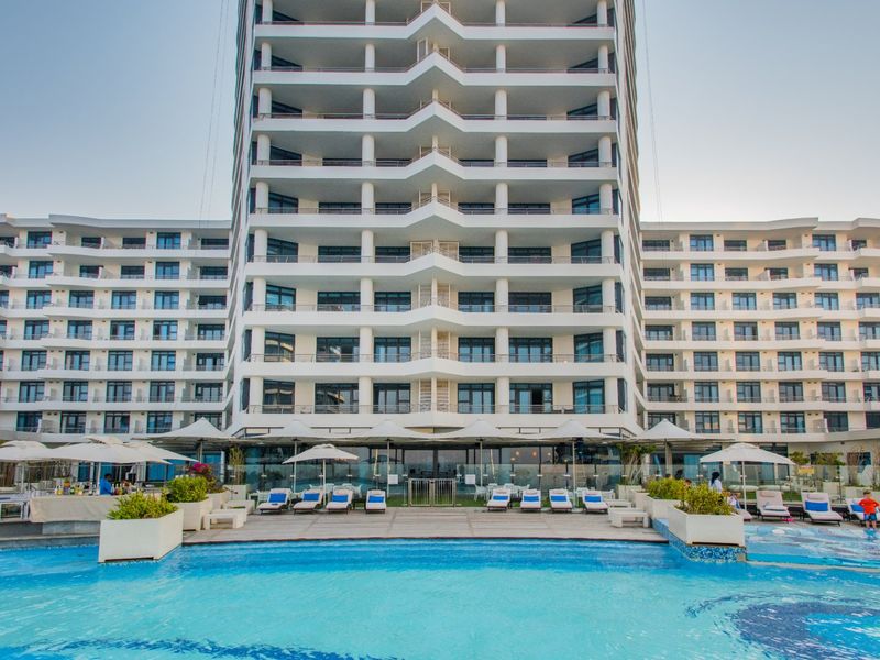 A view of a modern high-rise apartment building featuring multiple levels of balconies overlooking a well-maintained swimming pool and deck area.