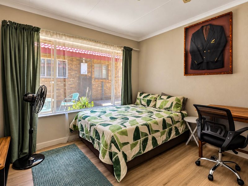 A well-lit bedroom featuring laminate flooring, a large window with garden views, and neutral wall finishes.