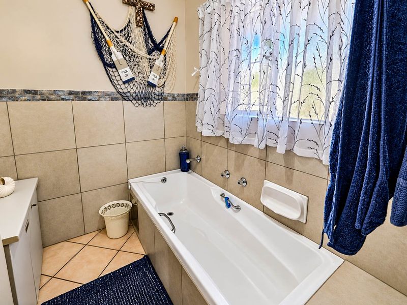 A functional bathroom featuring a built-in bathtub with wall-mounted fixtures, neutral wall tiling, and a vanity cabinet.