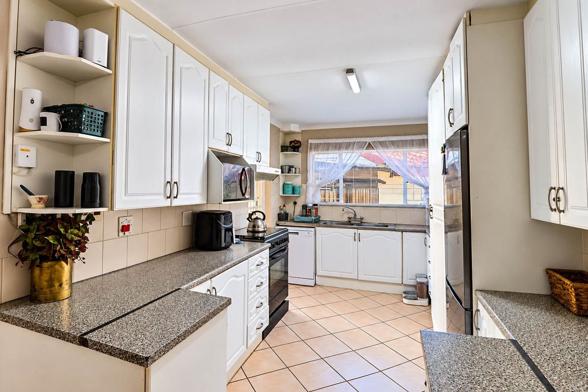 A functional kitchen featuring white cabinetry, laminate countertops, tiled flooring, and a tiled backsplash, offering a practical layout with ample storage space.