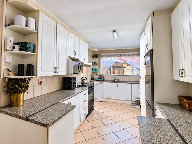 A functional kitchen featuring white cabinetry, laminate countertops, tiled flooring, and a tiled backsplash, offering a practical layout with ample storage space.