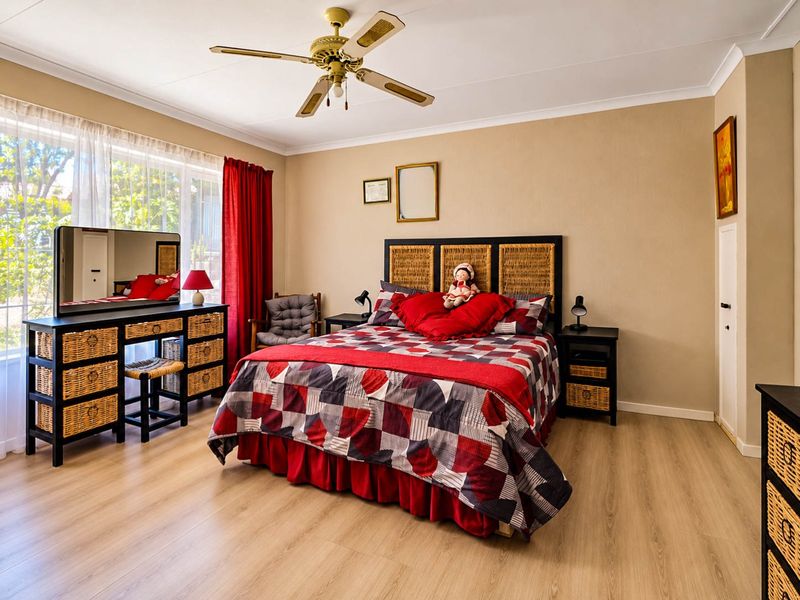 A well-maintained bedroom featuring light-toned laminate flooring, a ceiling fan, and large windows that provide ample natural light.