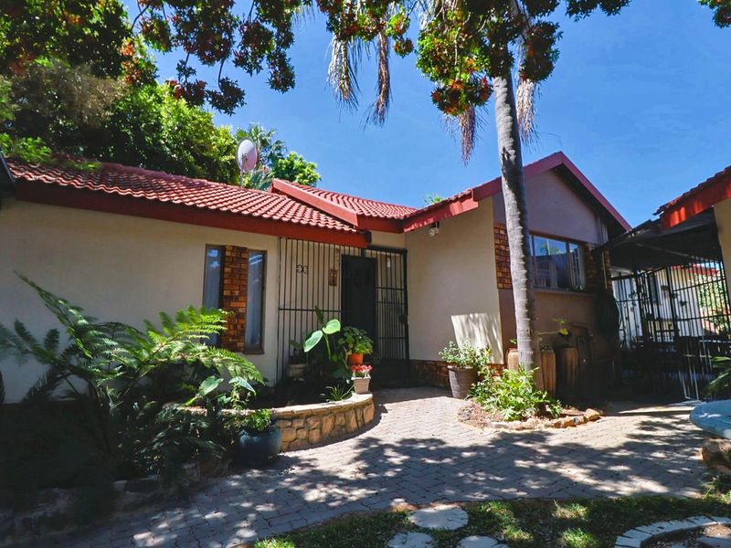 Front elevation of a single-story house featuring a tiled roof, brick accents, and a paved entrance area with established garden landscaping.