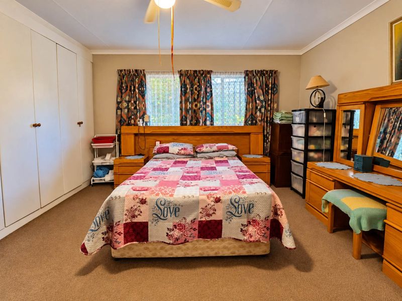 Spacious bedroom featuring neutral walls, carpeted flooring, built-in cupboards, and a ceiling fan, offering a functional and comfortable living space.