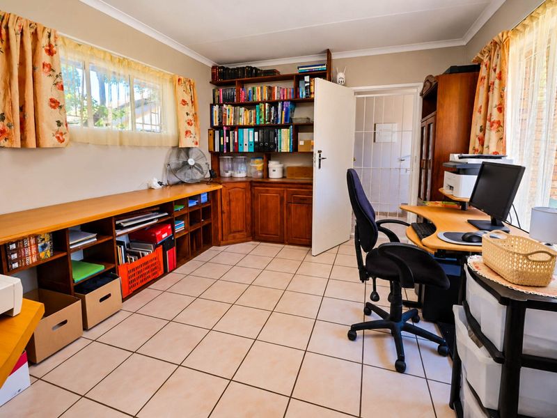 A functional home office featuring built-in wooden cabinetry, tiled flooring, and a security gate, providing a practical workspace with ample storage.