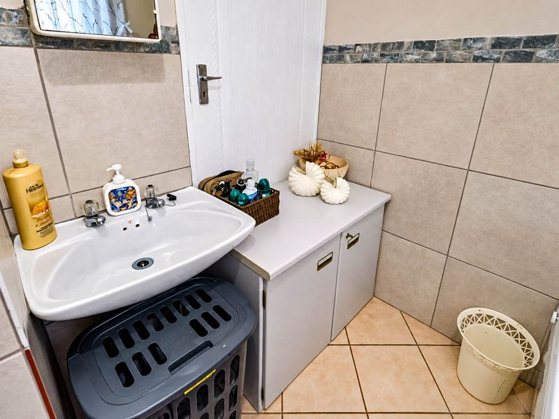 A functional bathroom featuring a wall-mounted basin, tiled walls with decorative border, and a built-in vanity cabinet for storage.