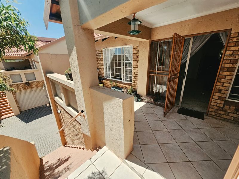 An elevated patio area featuring tiled flooring, a security gate, and access to the main entrance, overlooking the complex driveway and lower level.