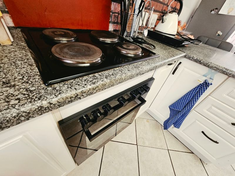 A kitchen area featuring granite countertops, a built-in oven, an electric hob, and white shaker-style cabinetry with tiled flooring.