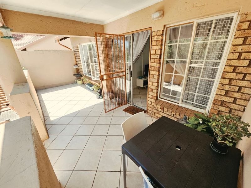 A covered patio area featuring tiled flooring, a security gate, and brick exterior walls, providing a functional outdoor space accessible from the living area.