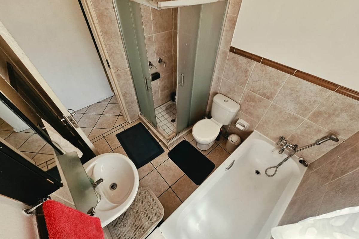 A functional bathroom featuring a separate shower enclosure, bathtub, toilet, and pedestal basin with neutral wall and floor tiling.