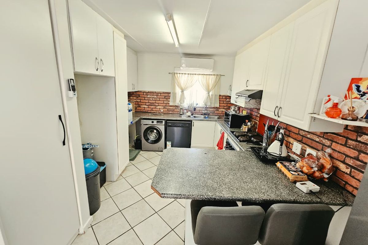 A functional kitchen featuring white cabinetry, granite countertops, a brick-style backsplash, and integrated appliances including a hob, oven, and extractor fan.