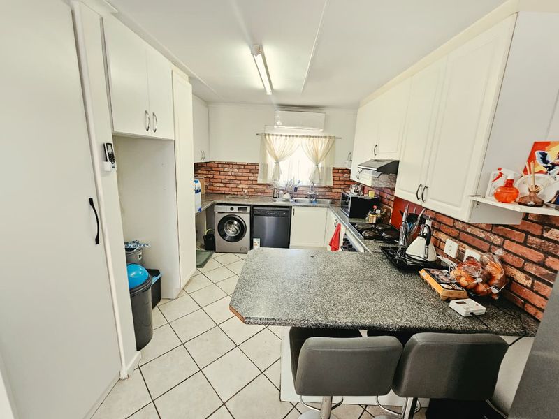 A functional kitchen featuring white cabinetry, granite countertops, a brick-style backsplash, and integrated appliances including a hob, oven, and extractor fan.