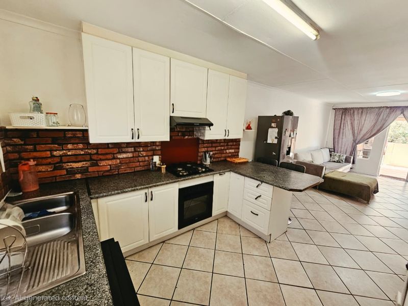 Open-plan kitchen and living area featuring white cabinetry, granite countertops, a gas hob, and a distinctive brick feature wall with tiled flooring throughout.