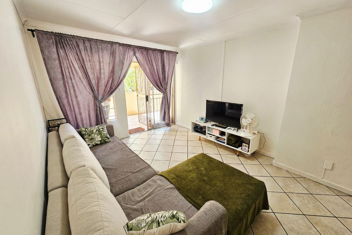 A bright living room featuring tiled flooring and a sliding glass door that provides access to an outdoor balcony area.