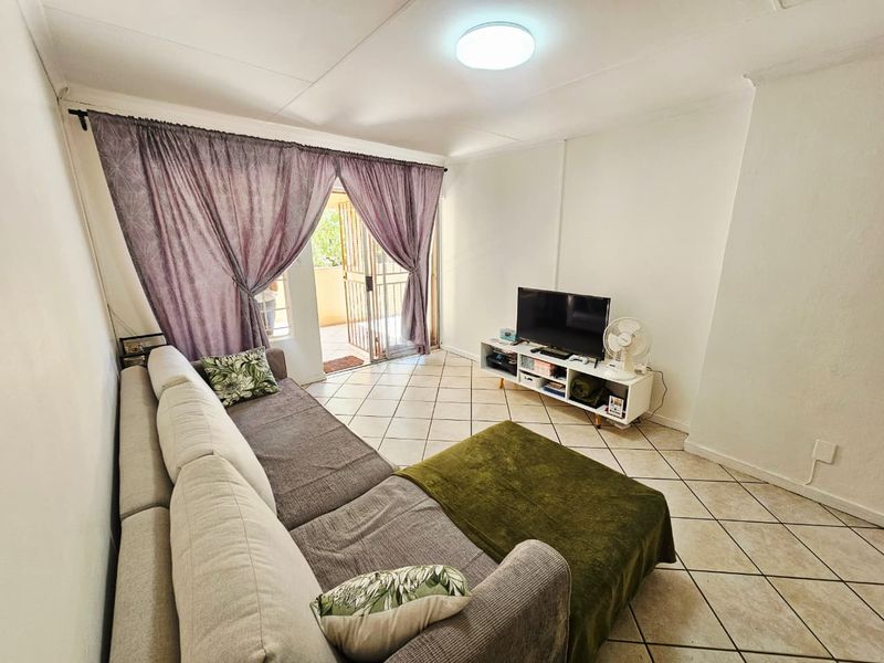 A bright living room featuring tiled flooring and a sliding glass door that provides access to an outdoor balcony area.