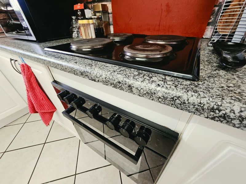 A kitchen area featuring a built-in oven, electric hob, granite countertops, and tiled flooring.
