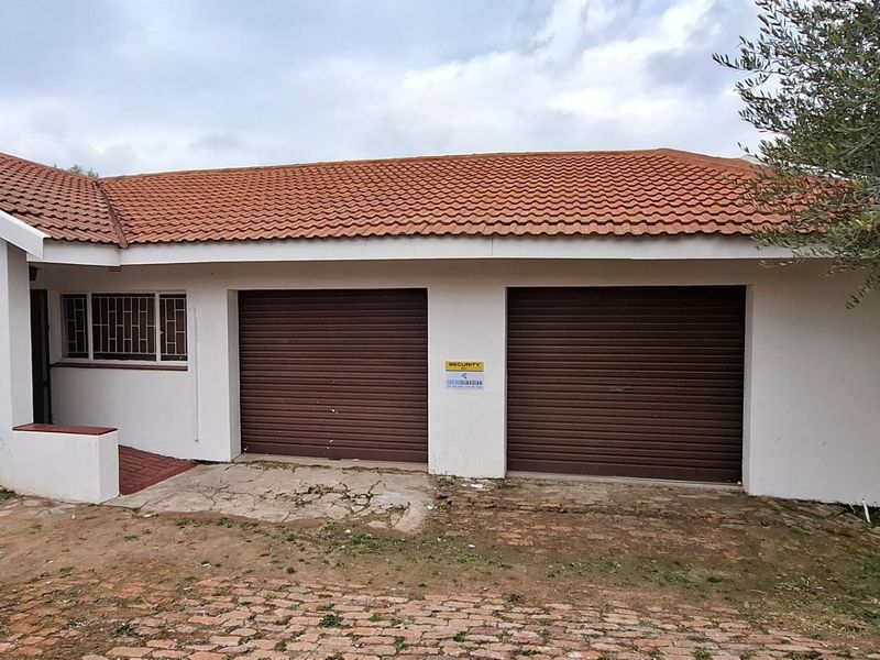 Front elevation of the property featuring a double garage with roller doors, tiled roof, and security bars on the windows.