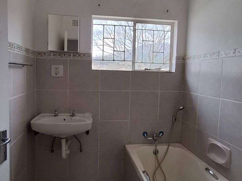 A functional bathroom featuring a wall-mounted basin, built-in bathtub with handheld shower, and neutral wall tiling. The space is ready for cosmetic updates.