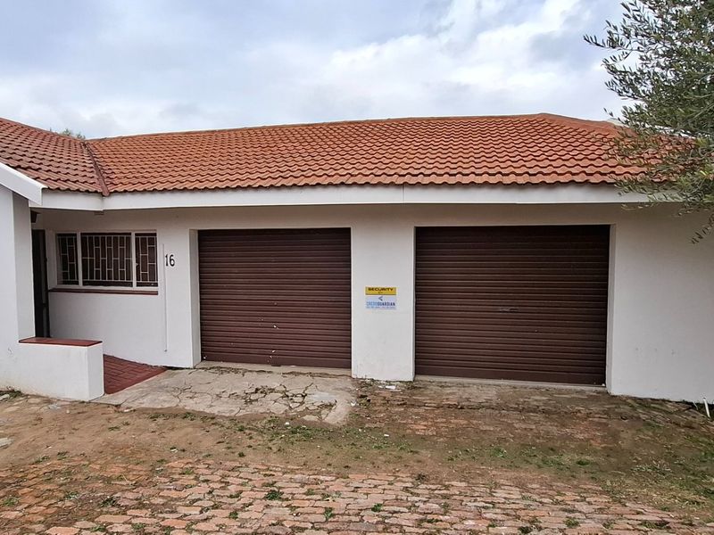 Front elevation of a residential property featuring a double garage with roller shutter doors, tiled roof, and security bars on windows.