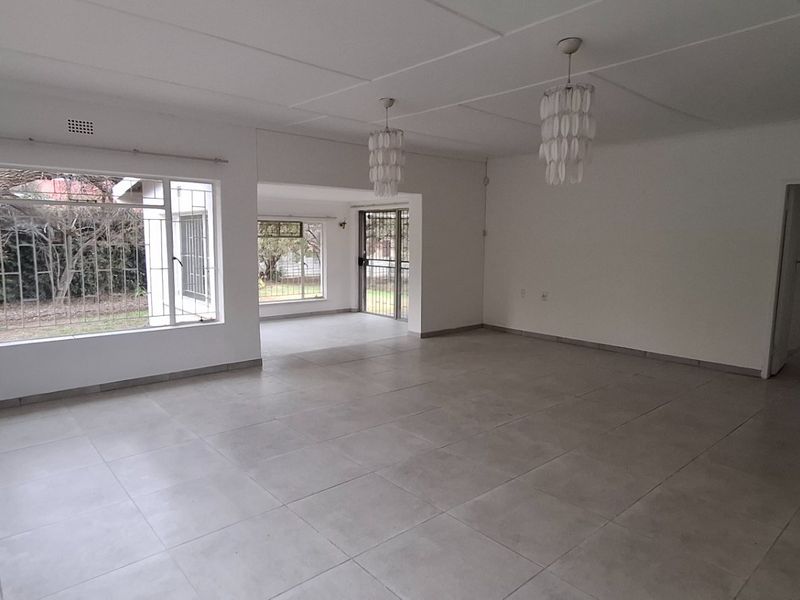 Spacious, open-plan living area featuring neutral tiled flooring, large windows with security bars, and direct access to the outdoor area.