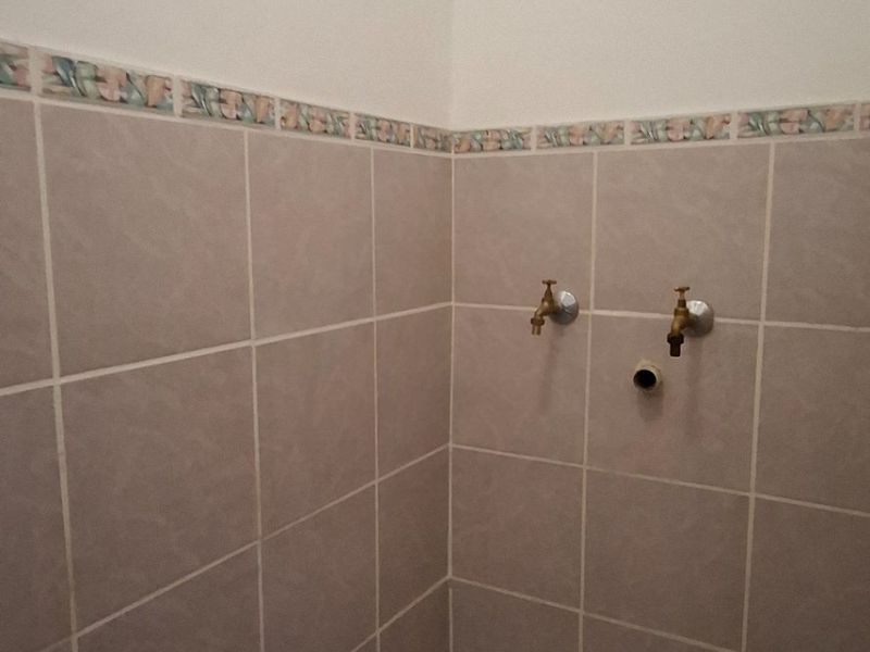 A functional laundry area featuring tiled walls with a decorative border, floor tiling, and dedicated plumbing connections for a washing machine.