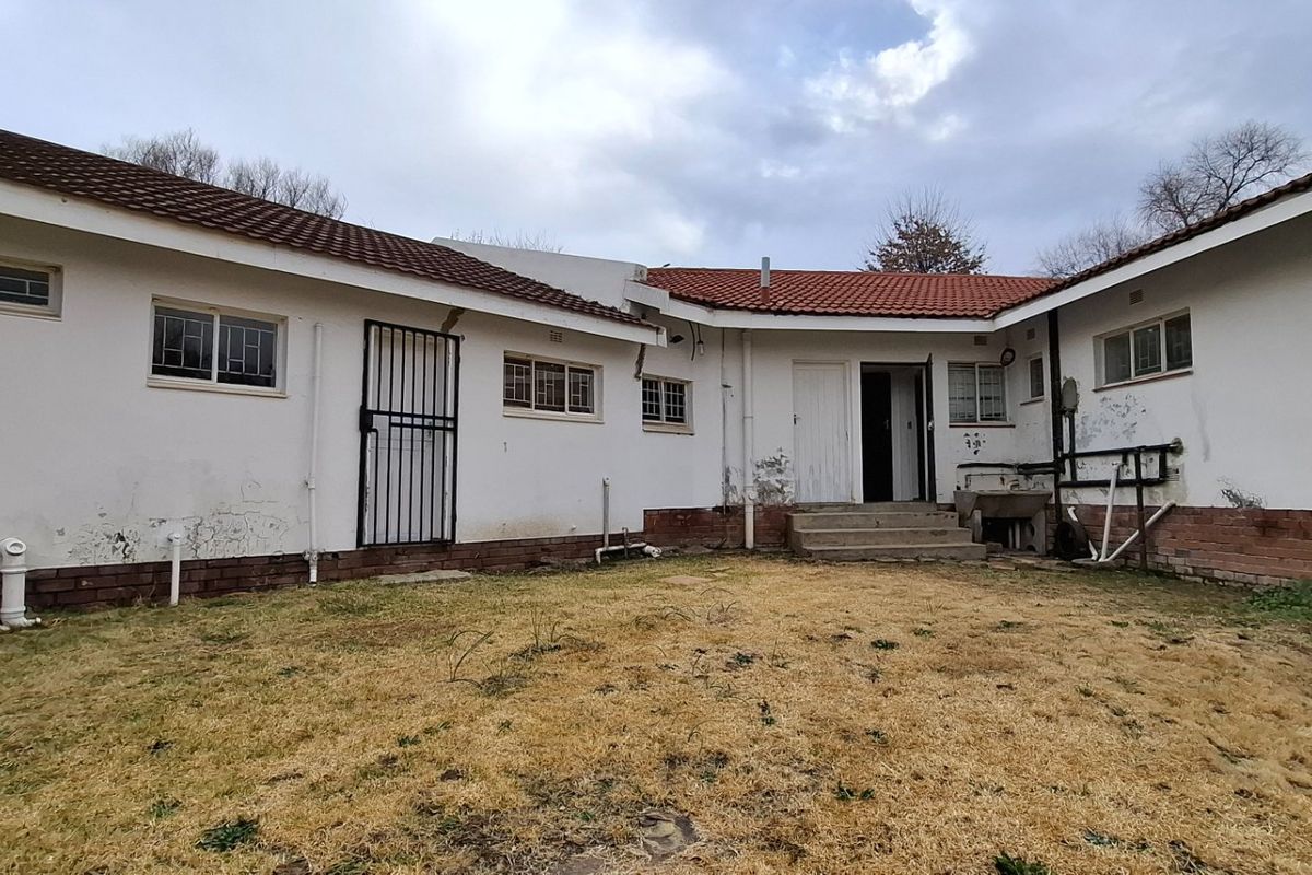 Rear view of the property showing the exterior facade, tiled roof, and garden area with visible signs of wear and maintenance requirements.