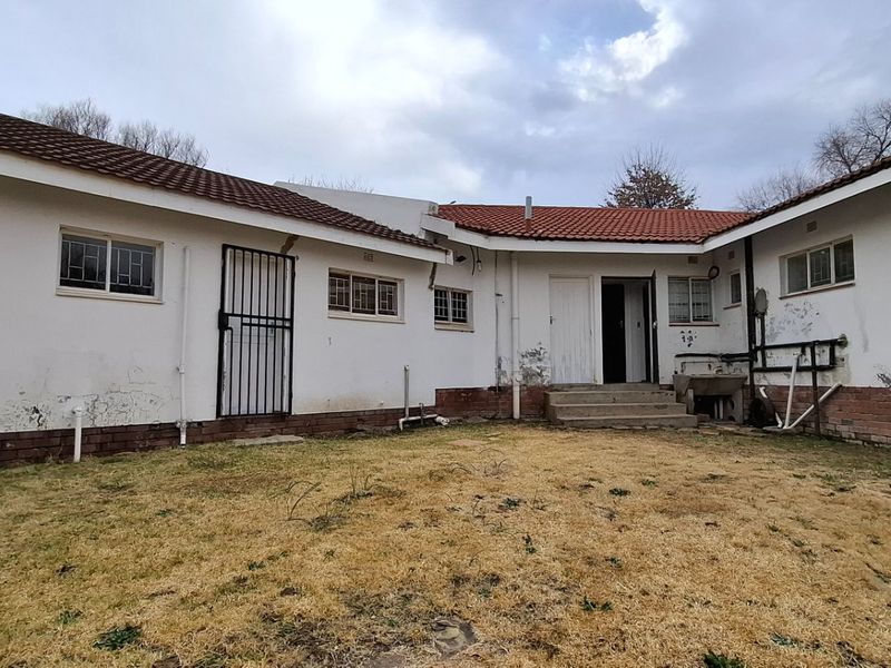 Rear view of the property showing the exterior facade, tiled roof, and garden area with visible signs of wear and maintenance requirements.