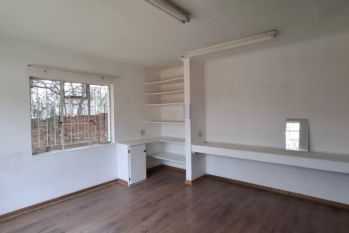 An empty bedroom featuring laminate flooring, built-in shelving, and a built-in desk area with security bars on the window.
