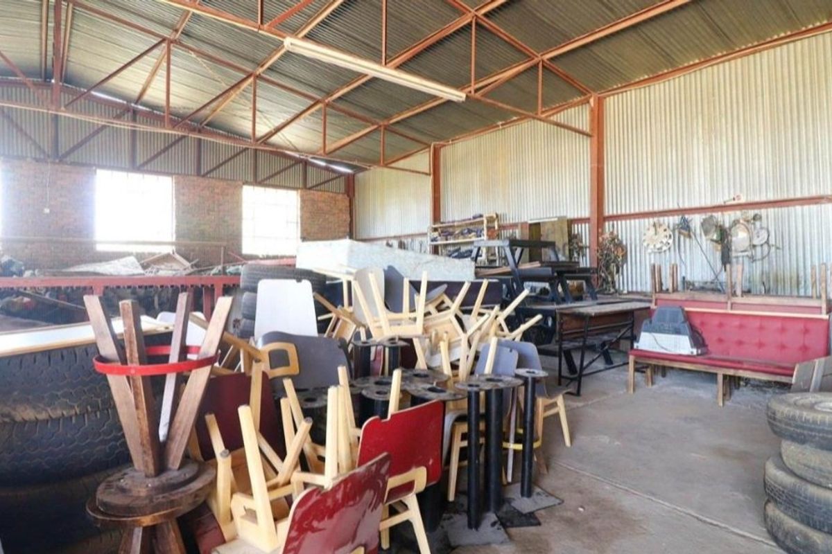 Large industrial utility space featuring exposed steel roof trusses, corrugated iron wall cladding, and a concrete floor, suitable for storage or workshop use.