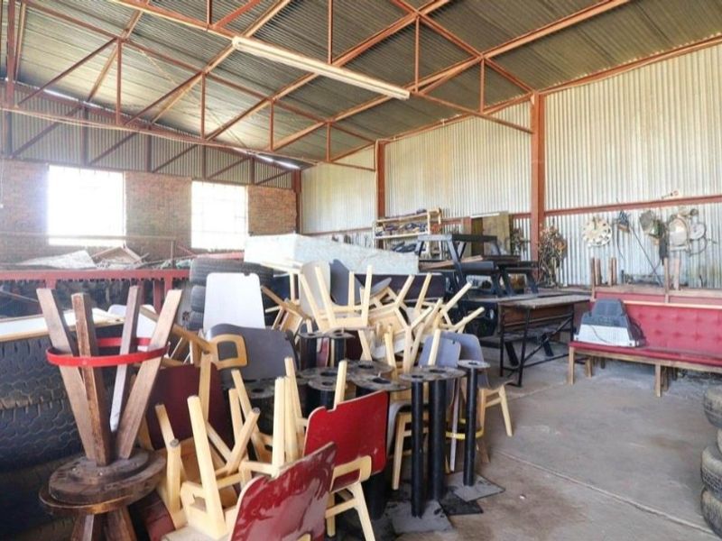 Large industrial utility space featuring exposed steel roof trusses, corrugated iron wall cladding, and a concrete floor, suitable for storage or workshop use.