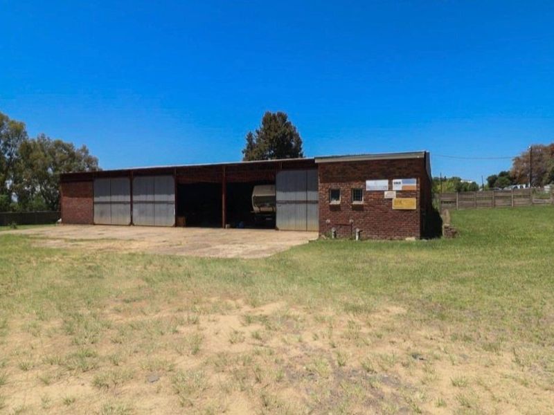 Industrial property featuring a brick-constructed shed with large sliding metal doors and a concrete apron, set on a spacious open plot.