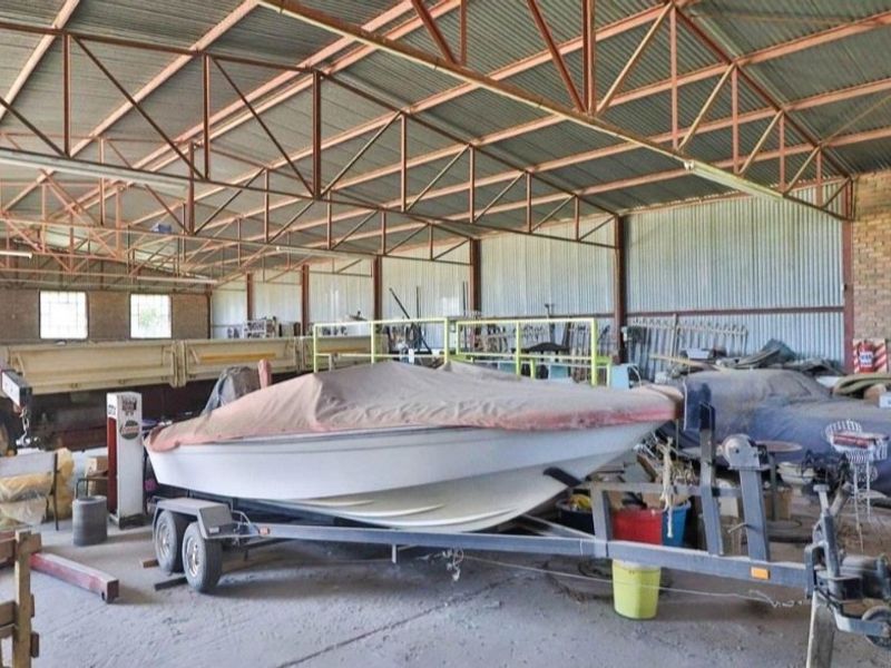 Spacious industrial-style garage featuring exposed steel roof trusses, corrugated metal wall cladding, and durable concrete flooring, suitable for large-scale storage or workshop use.