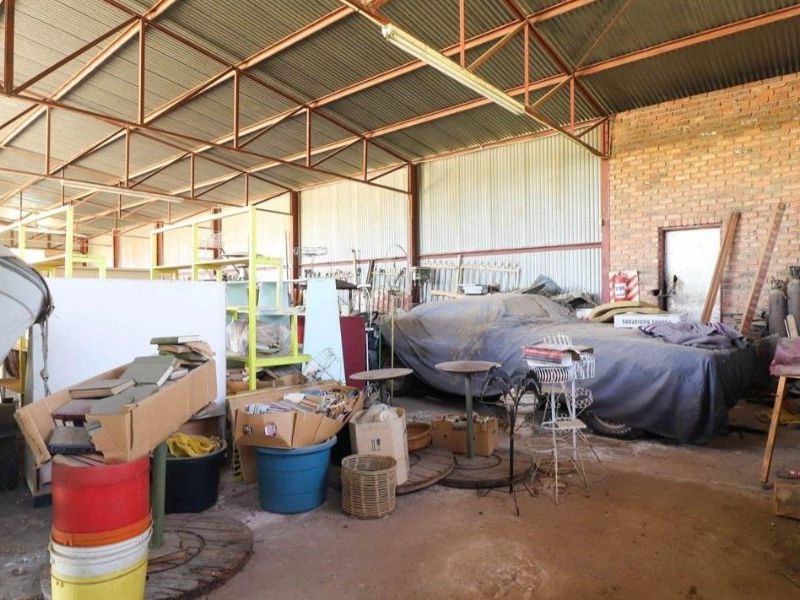 Spacious industrial garage featuring exposed steel roof trusses, corrugated metal cladding, and exposed brickwork, providing ample storage or workshop potential.
