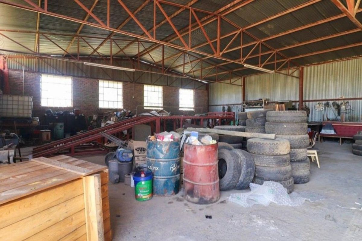 Spacious industrial utility area featuring exposed steel roof trusses, corrugated metal cladding, brick walls, and durable concrete flooring, suitable for workshop or storage use.