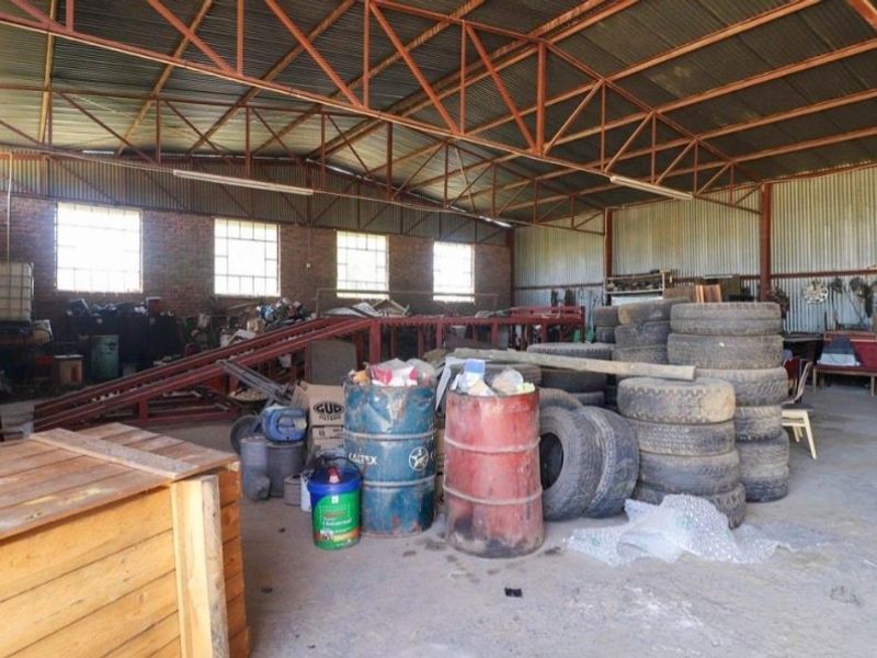 Spacious industrial utility area featuring exposed steel roof trusses, corrugated metal cladding, brick walls, and durable concrete flooring, suitable for workshop or storage use.